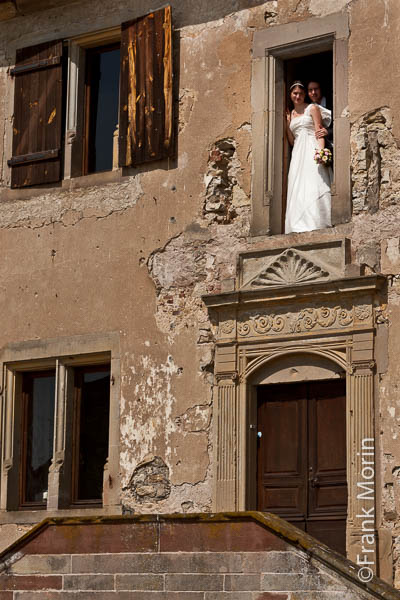Les mariés dans le château, debouts à une fenêtre, photographiés depuis l'extérieur