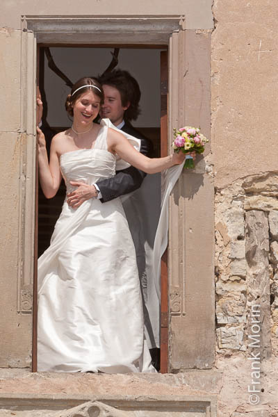 Les mariés dans le château, debouts à une fenêtre, photographiés depuis l'extérieur