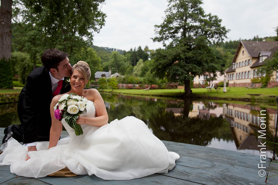 Les mariés au bord d'un étang, l'homme dépose un baiser à la tempe de sa fiancée