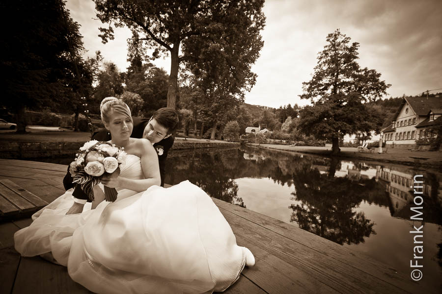 En Noir et Blanc, les mariés au bord d'un étang, l'homme dépose un baiser sur l'épaule de sa fiancée