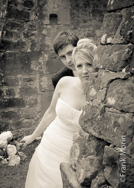 En noir et blanc dans un décor de batiment en ruine, les mariés regardent vers l'appareil photo