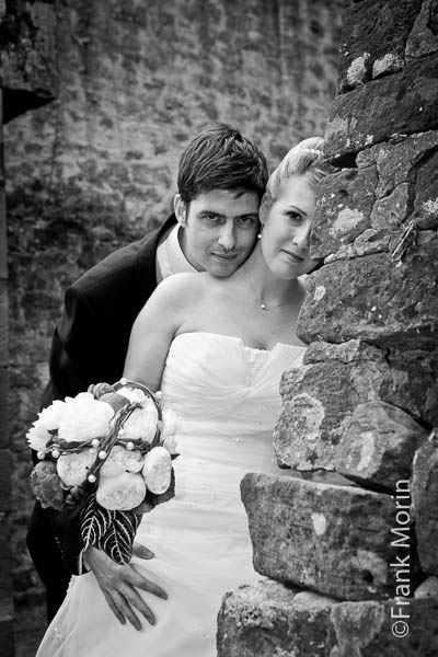 En noir et blanc dans un décor de batiment en ruine, les mariés regardent vers l'appareil photo