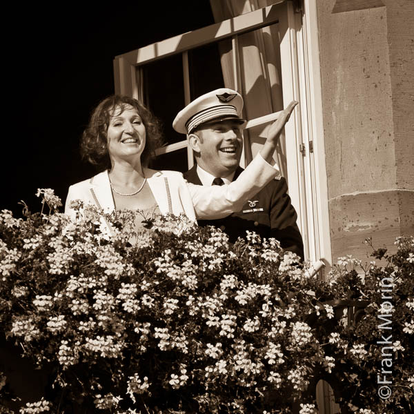 les Mariés saluent les invités derrière les fleurs du balcon de la mairie.