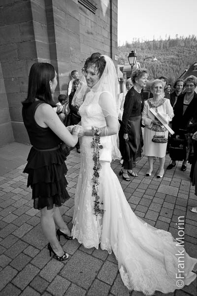 sous le porche de l'église, une amie serre les mains de la Mariée pour la féliciter.