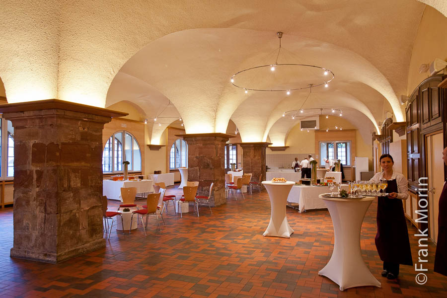 Salle préparée pour l'apéritif. Une serveuse attend avec un plateau de verres de crément. Les voutes du plafond sont soutenues par de gros piliers carrés