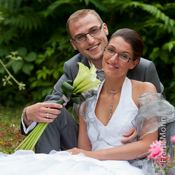 Les fiancés assis au milieu des fleurs regardent vers l'appareil photo.