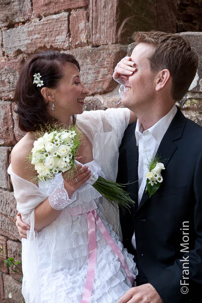 La mariée assise sur les genoux de son fiancé lui masque les yeux de la main.