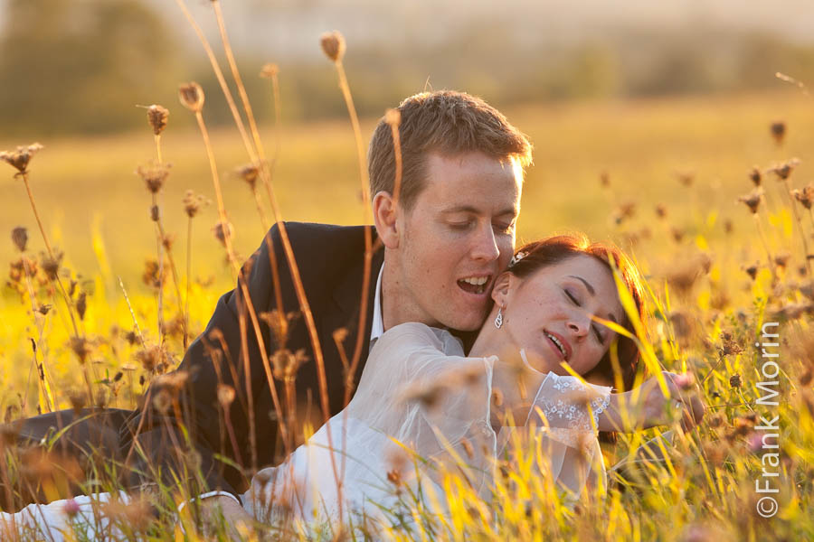 Les mariés s'embrassent, couchés dans l'herbe sous le soleil couchant