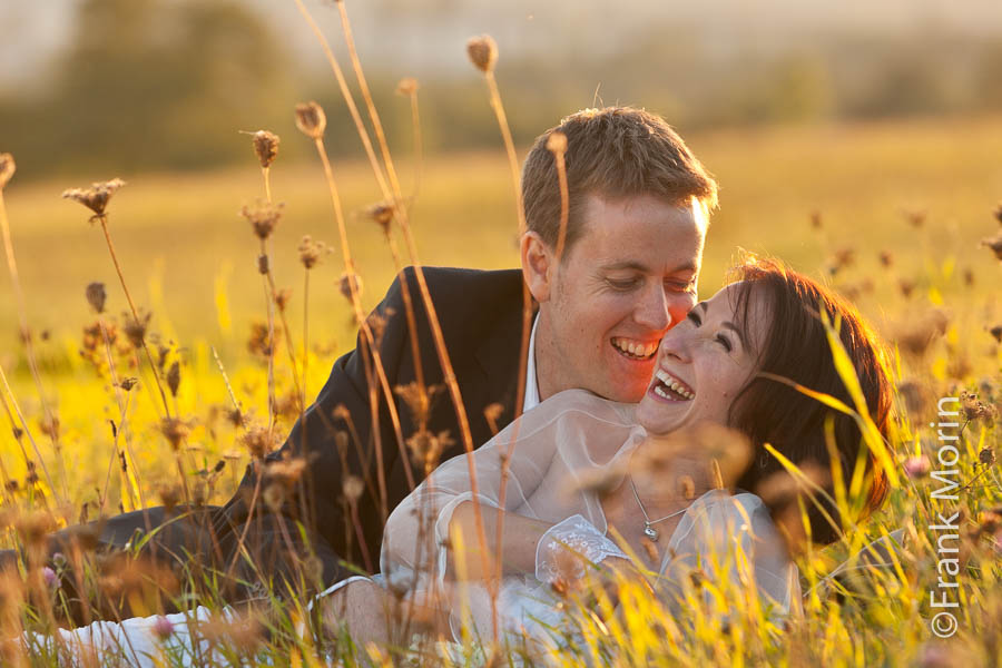 Les mariés s'embrassent en riant, couchés dans l'herbe sous le soleil couchant